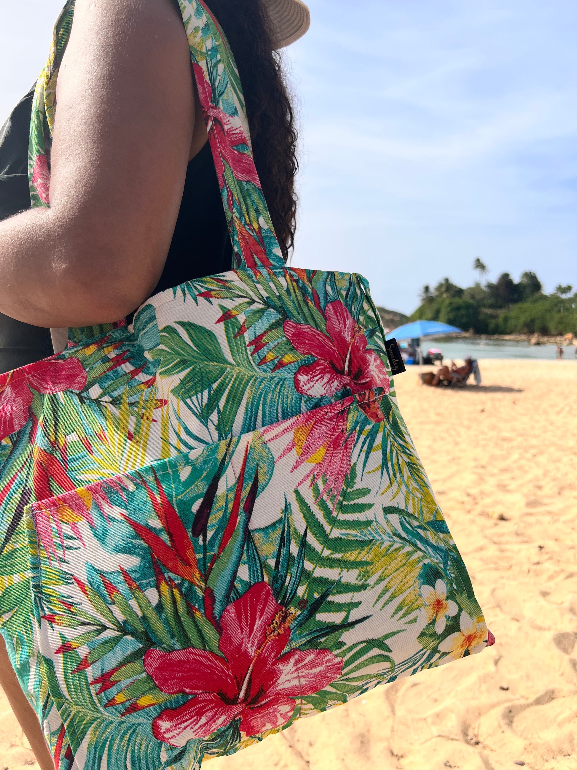 woman carrying red floral beach tote holding towel sunscreen and sunglasses